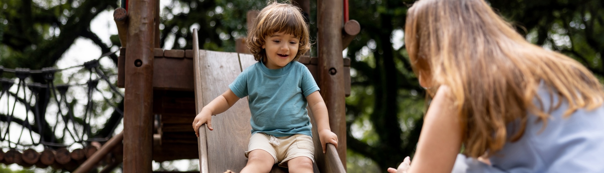 Moeder kijkt naar jong kind op glijbaan: kinderen overbeschermen