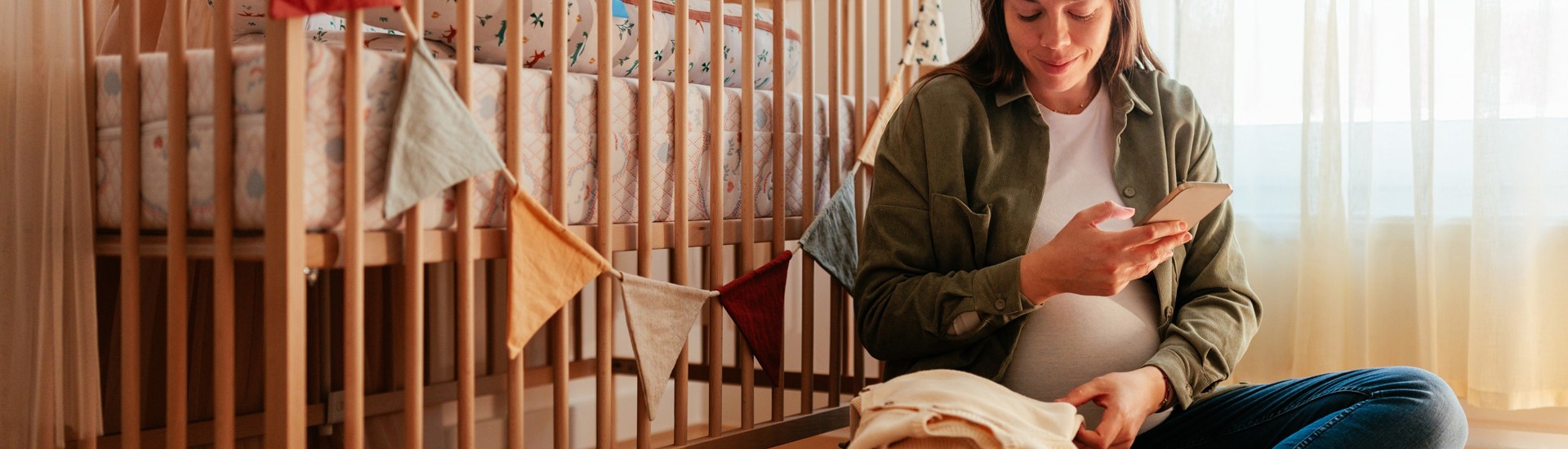 Zwangere vrouw met smartphone in babykamer - Vroedvrouw opzoeken